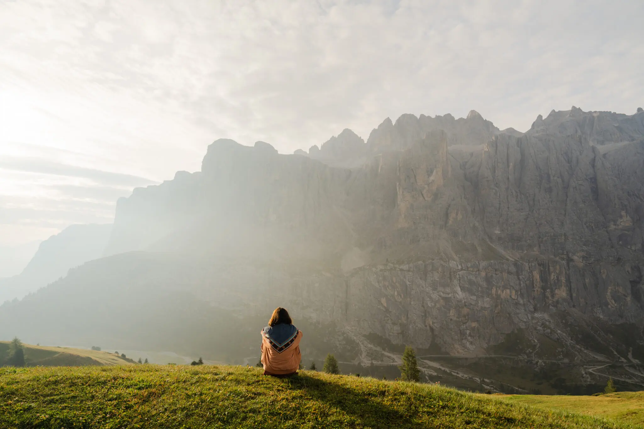Person sitting on grassy hill facing mountains