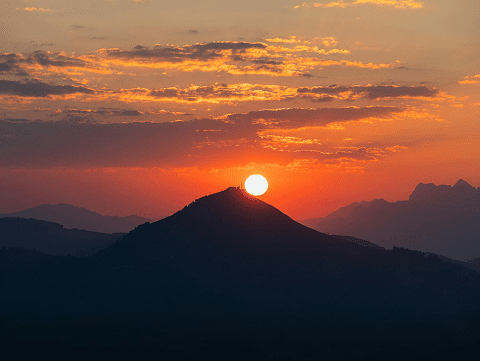 Sun setting behind silhouetted mountain peak